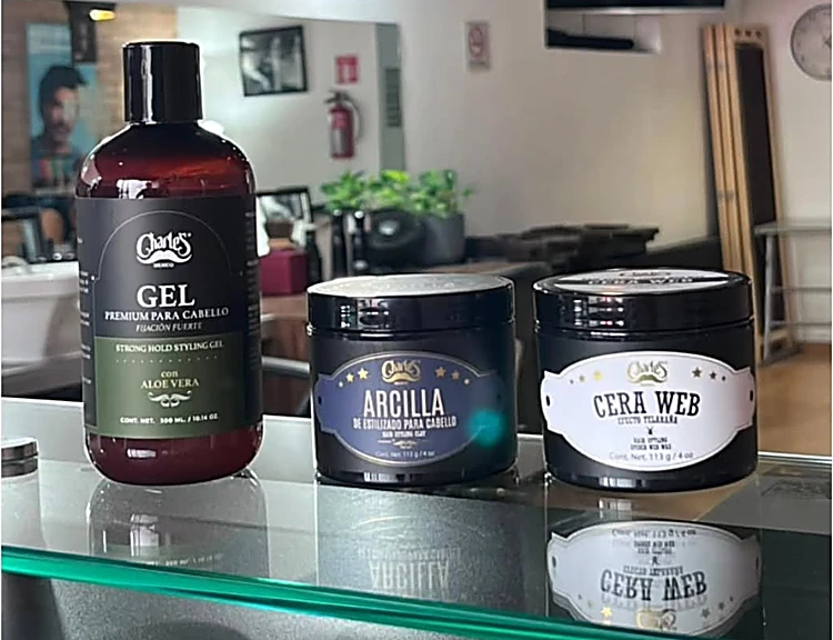 Gel, arcilla y cera web Charles sobre el mostrador de vidrio de canto verde, con el local al fondo.